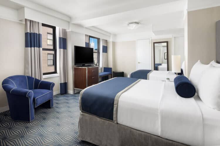 A hotel room with a bed, chair, TV, and window