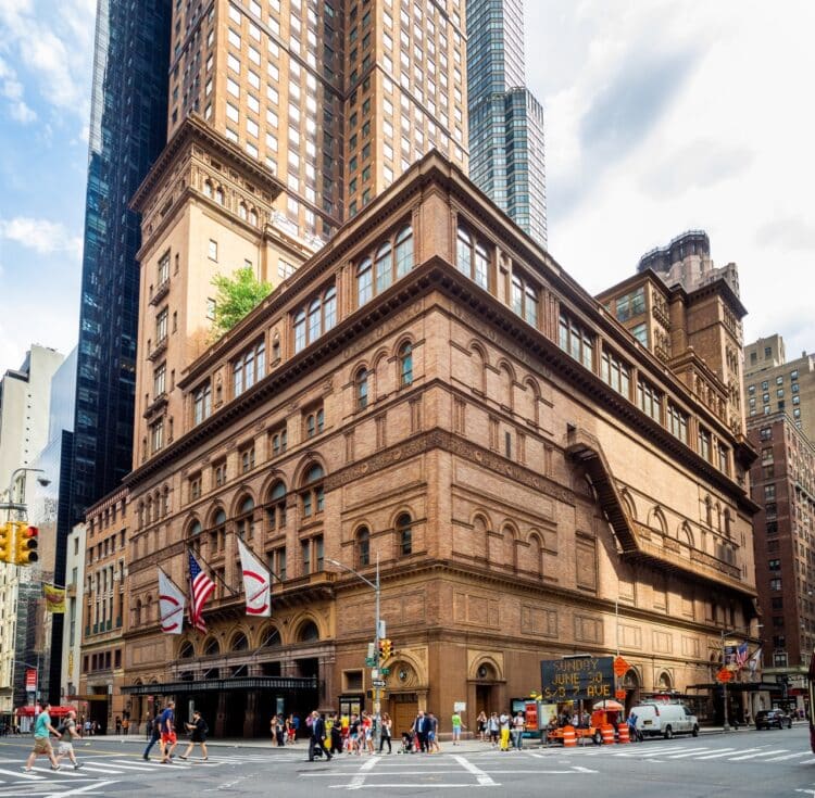 A wide-angle view of a large brownstone building in a city with people walking on the sidewalk.