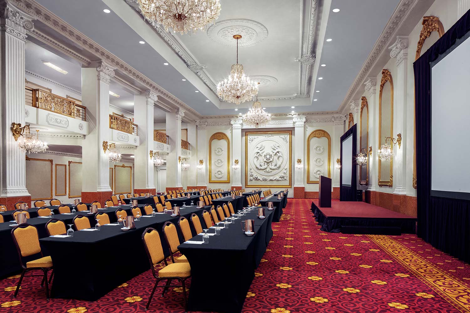 A large, ornate meeting room with a stage, tables, and chairs.