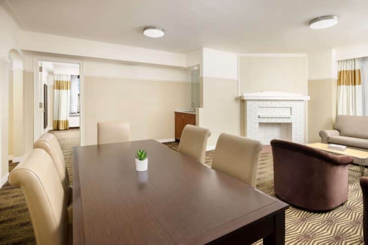A wide view of a hotel room with a dining table, sitting area, and fireplace.