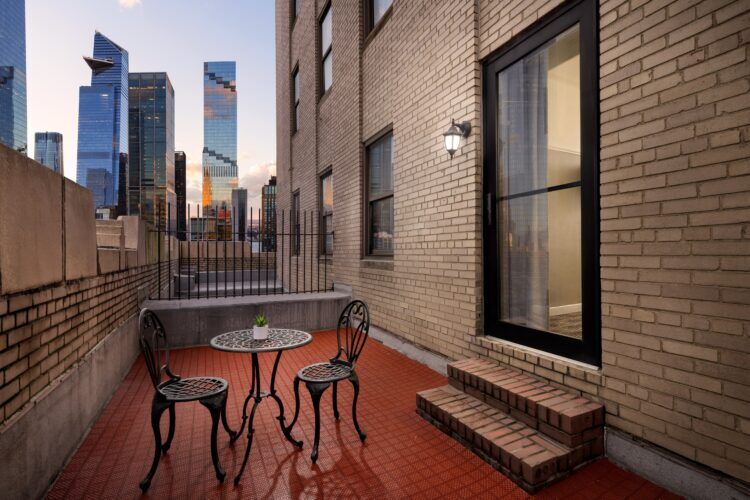 A small outdoor terrace with a table and chairs on a red tile floor, overlooking the city skyline.