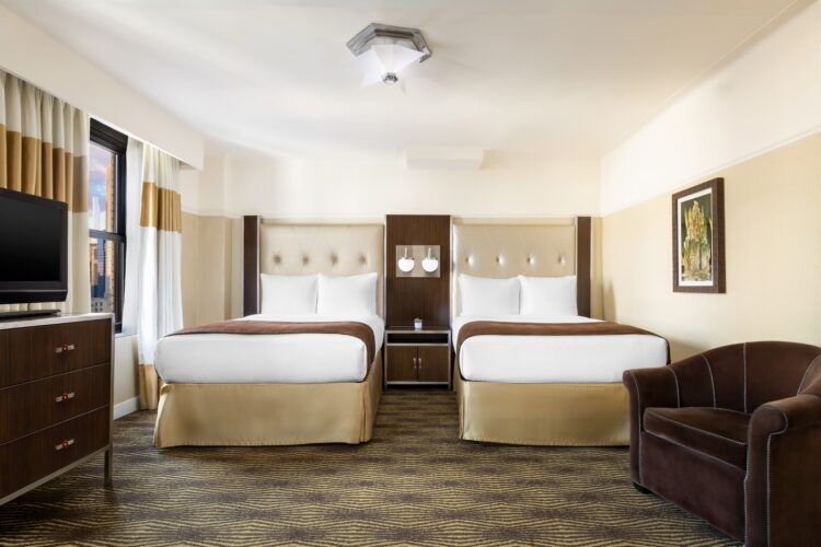 A hotel room with two beds, a window, and a TV on a dresser.