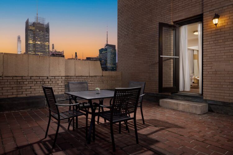 A rooftop terrace with a table and chairs overlooking the city skyline at sunset.