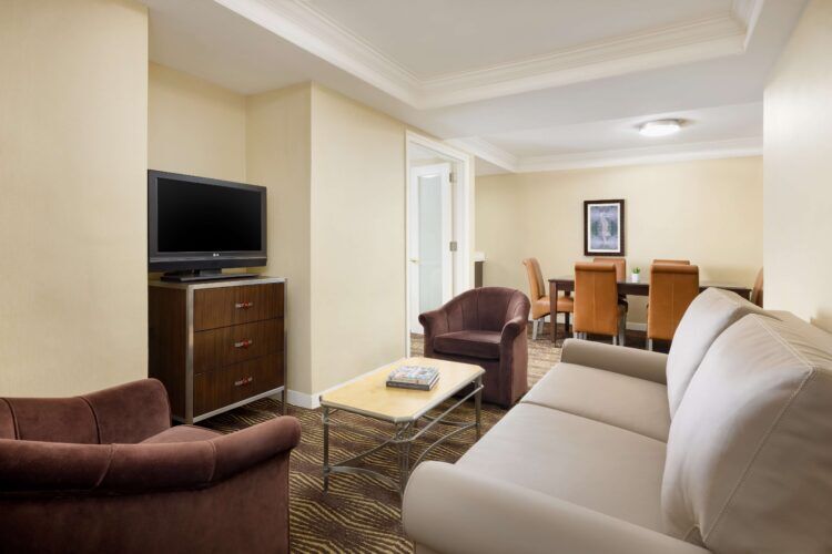 A wide view of a hotel suite with a sofa, armchairs, a TV, and a dining table.