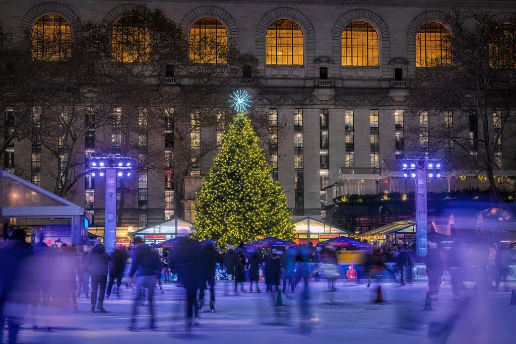 a large Christmas tree in front of a building with people ice skating