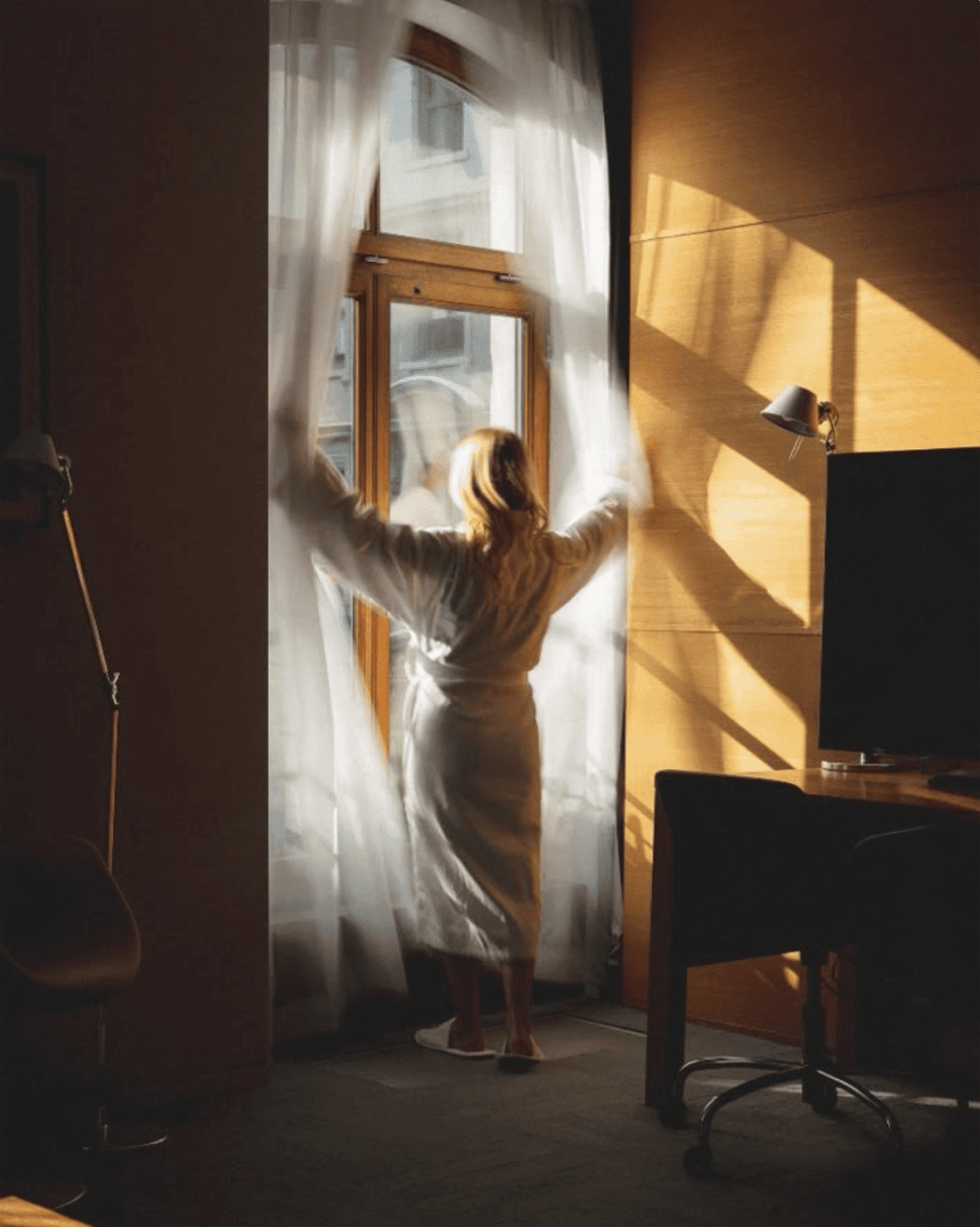 woman opening large windows in hotel with sun shining whilst wearing robe in nyc